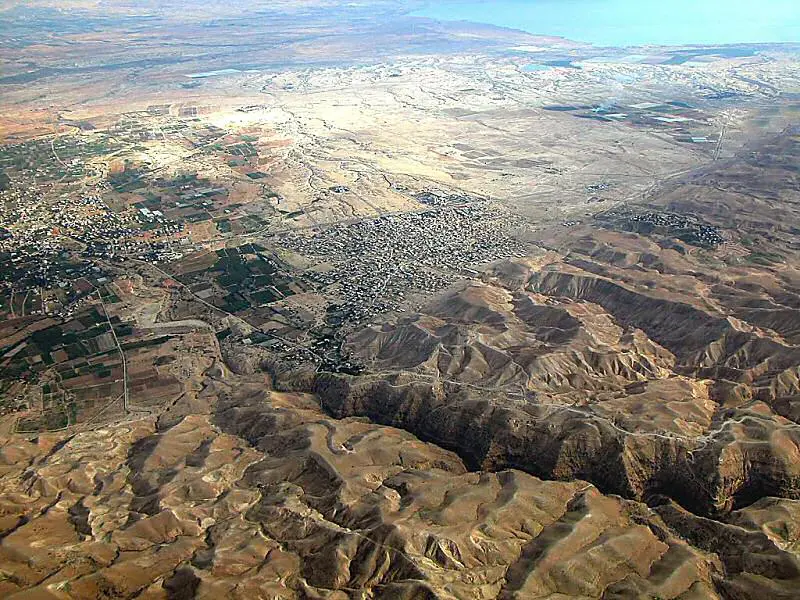 Jericho From The Northwest. From Herod's palace, the road begins a quick and difficult ascent into the Judean wilderness. Known biblically as the "Ascent of Adumim," this road travels on the southern side of the Wadi Qilt (Josh. 15:7). In the photo, the Wadi Qilt is the deep gorge running diagonally from the lower right corner and the Ascent of Adumim can be seen just above it. Herod's palaces are located where the Wadi Qilt enters the Jordan Valley, and the Dead Sea is 6 miles (10 km.) south. The root of "Adumim" means "red," and the plural may be translated as "red places." The name most likely comes from the red earth that appears along the route.
