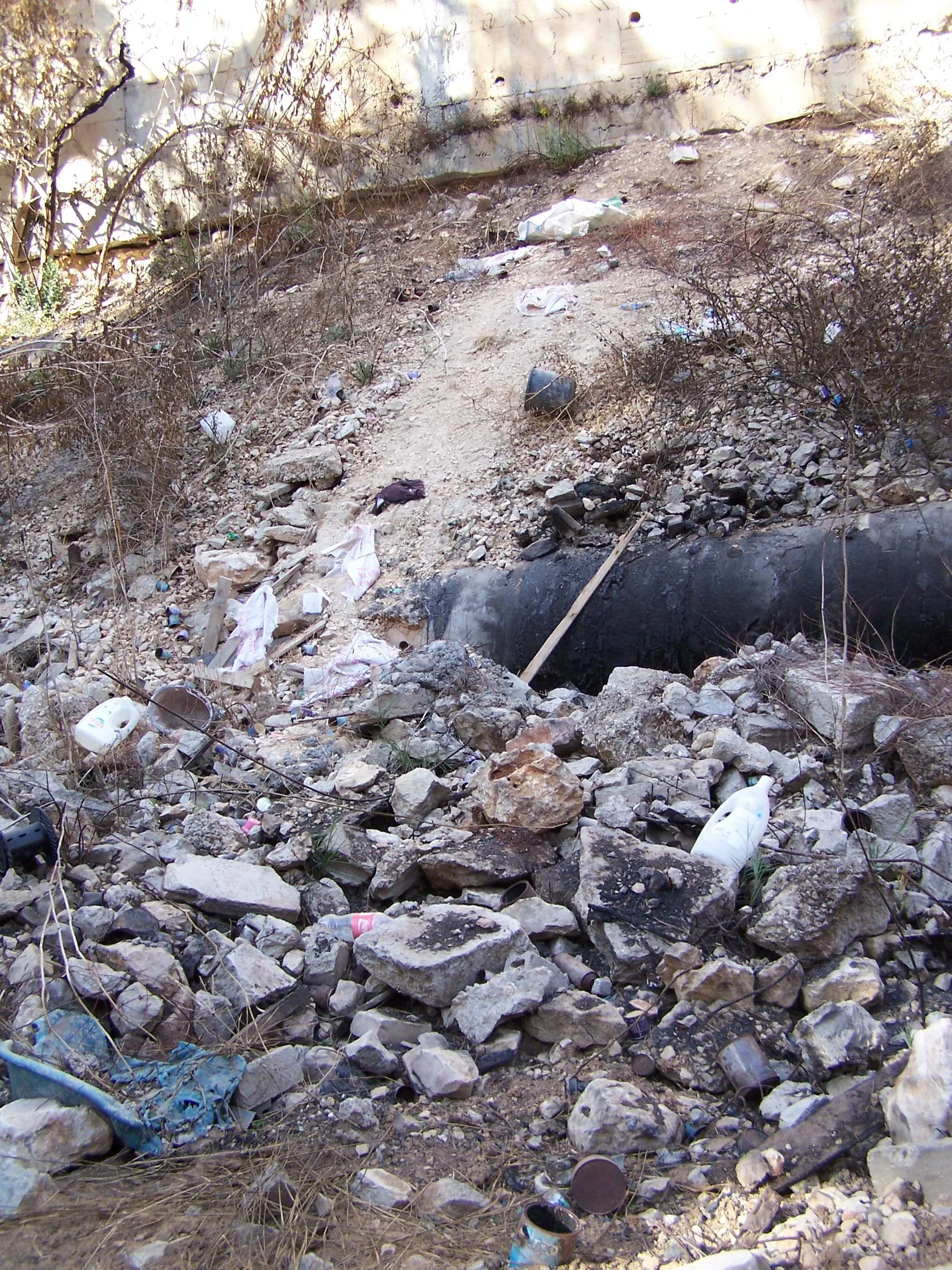Rubble, refuse and other debris from the Har Hamenuhot cemetery above have tumbled into the valley where the Roman road to Emmaus once ran, partially covering the water main that was blackened in a recent fire. Photographed by Joshua N. Tilton, November 12, 2016.