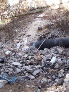 Rubble, refuse and other debris from the Har Hamenuhot cemetery above have tumbled into the valley where the Roman road to Emmaus once ran, partially covering the water main that was blackened in a recent fire. Photographed by Joshua N. Tilton, November 12, 2016.